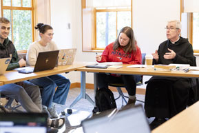 A priest speaks to a classroom. Links to Gifts That Pay You Income